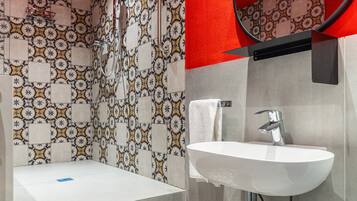 A bathroom with a patterned tile wall, a white sink, a mirror, and a bathtub.
