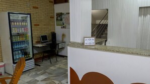 A reception area with a computer, a refrigerator stocked with beverages, and a staircase leading to an upper level. - Hotel Jóia (Cascavel)
