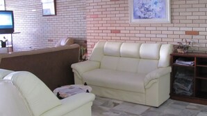 A living room with a beige sofa, a smaller armchair, a coffee table, and a brick-patterned wall with a framed picture. - Hotel Jóia (Cascavel)