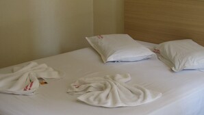 A neatly made bed with white linens and pillows, a wooden headboard, and a plain wall. - Hotel Jóia (Cascavel)