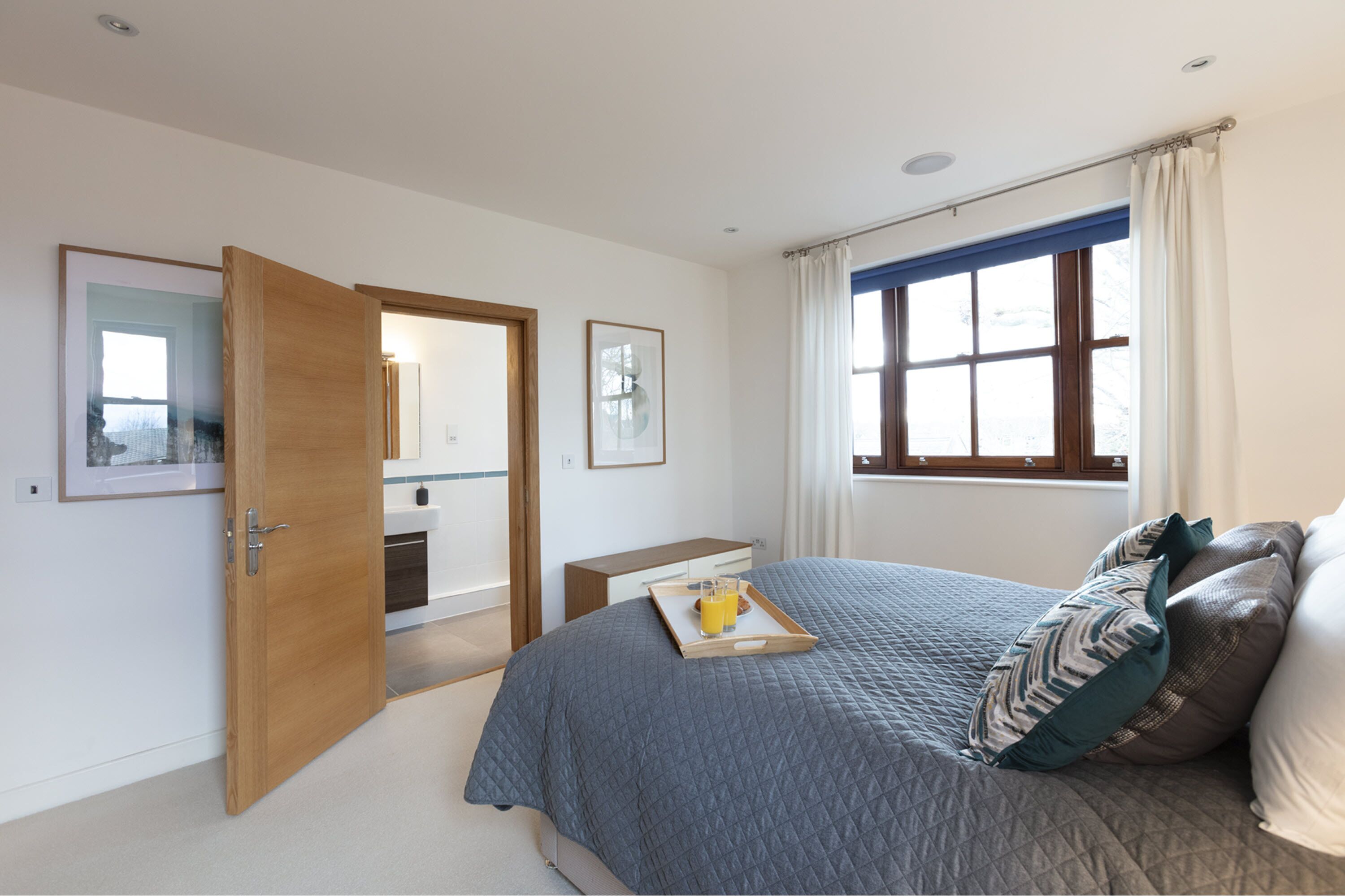 A bedroom with a bed, a bedside table, a tray with a glass of orange juice, and a window with curtains.