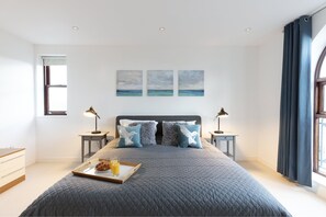 A bedroom with a large bed, two bedside tables, a tray with breakfast, and a view of the sea through the window. - Hampden Apartments - The Henry (Windsor)