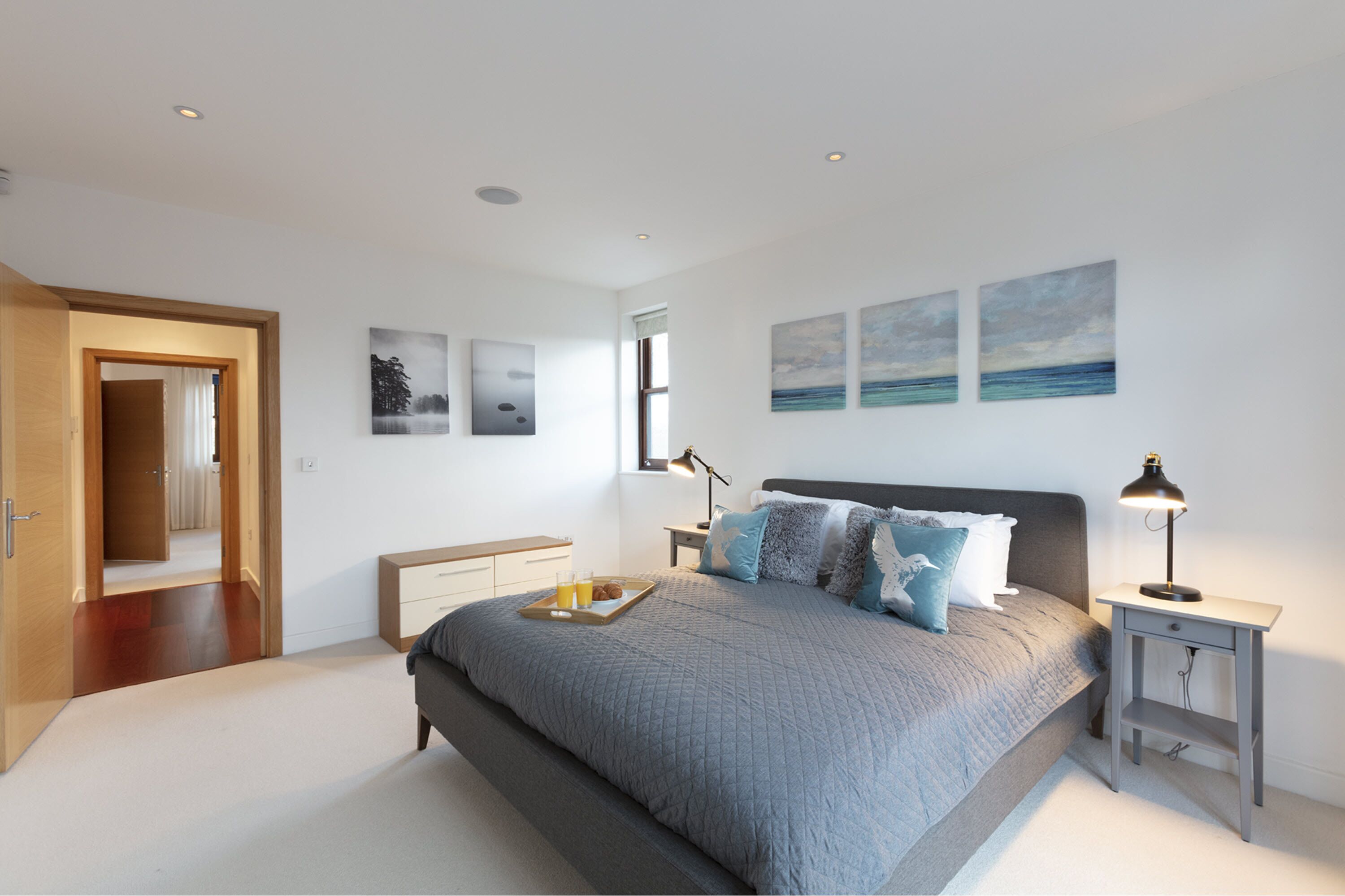 A modern bedroom with a large bed, a bedside table with a lamp, a nightstand, and a tray with breakfast items.