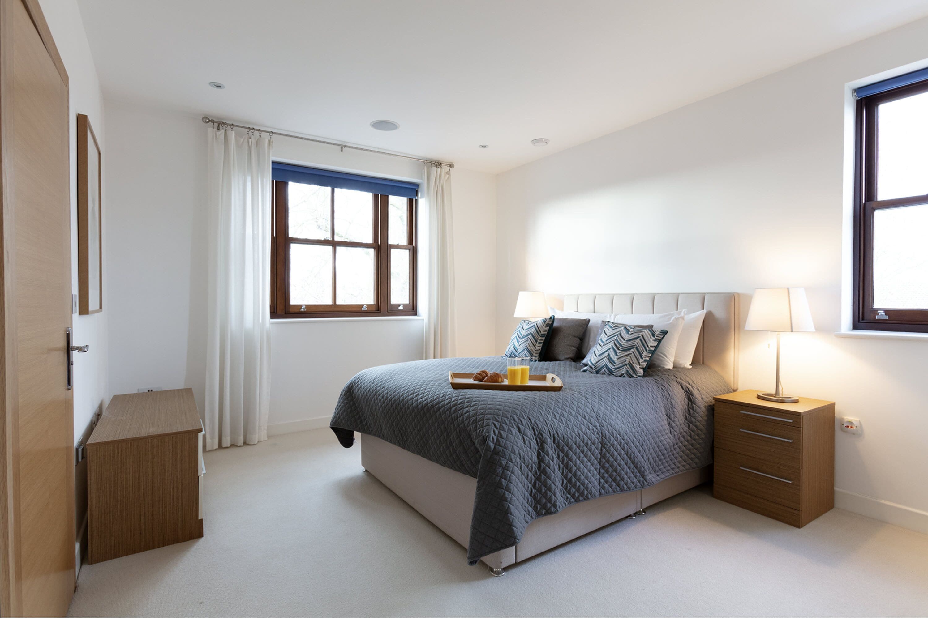 Un dormitorio con cama, mesitas de noche, una ventana y cortina.