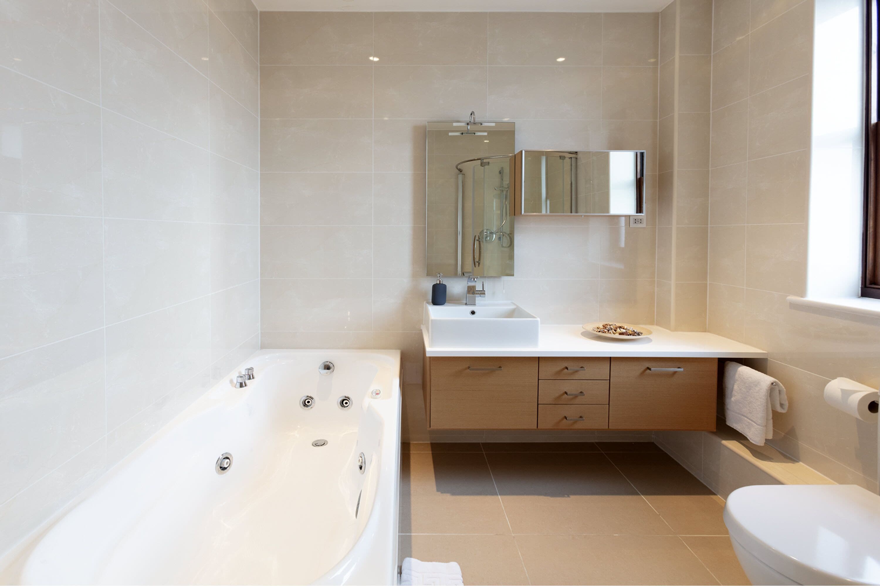 A modern bathroom with a bathtub, sink, mirror, and toilet.