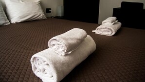 A neatly made bed with a brown quilt, two rolled white towels, and a white pillow. - Civico7 (Naples)