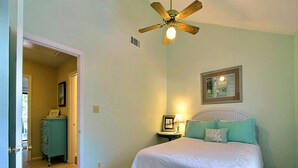 A bedroom with a bed, a ceiling fan, a nightstand with a lamp, and a framed picture on the wall. - Heated Pool Access | 5*Clean | Flex Cancelation (Tybee Island)