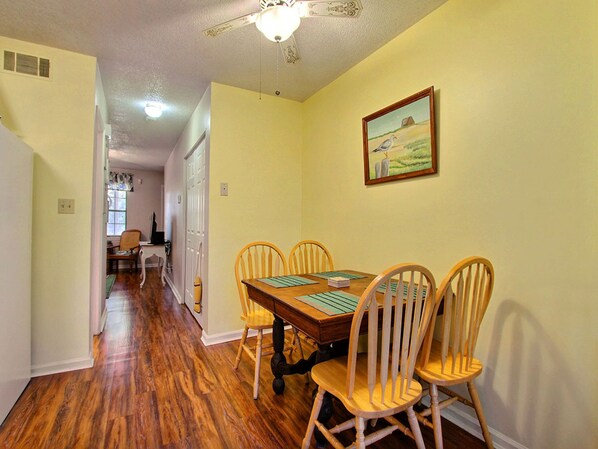 Un coin repas avec une table et des chaises en bois, un ventilateur de plafond et un tableau accroché au mur.