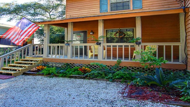A two-story wooden house with a front porch, steps, and a small garden area. - Heated Pool Access | 5*Clean | Flex Cancelation (Tybee Island)