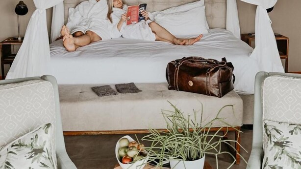Une chambre à coucher avec un lit à baldaquin, une table de chevet ornée d’une plante et deux fauteuils.