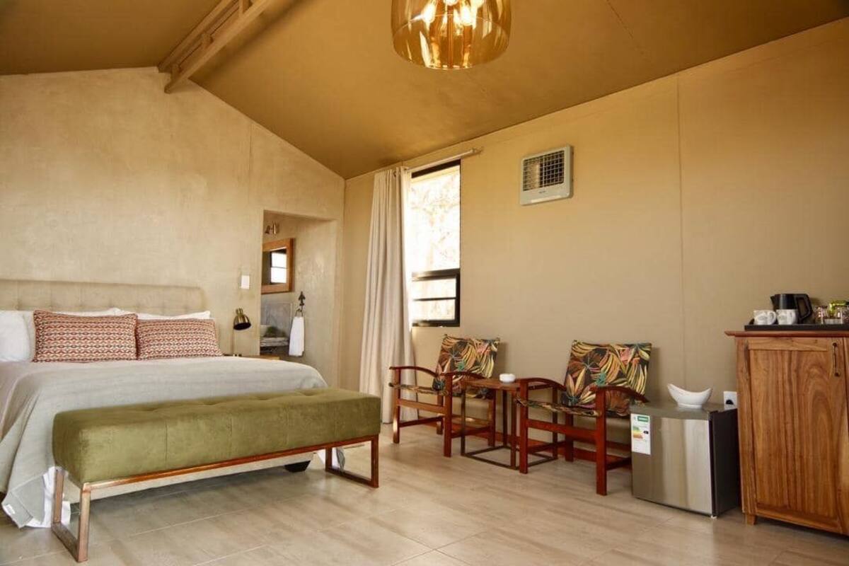 Ein Schlafzimmer mit einem Bett, einer Bank, zwei Stühlen, einem kleinen Tisch, einem Schrank und einem Fenster.