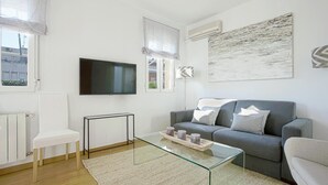 A modern living room with a grey sofa, a glass coffee table, a white chair, and a flat-screen TV mounted on the wall. - Beautifuly Decorated 2 Bd Apart With Private Terrace, Reina Sofia (Madrid)