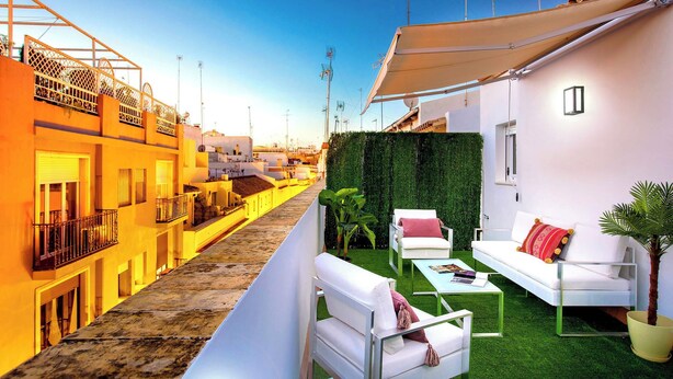 A modern outdoor living area with a white sofa, a small table, and a potted plant. - Genteel Home Galera II (Seville)