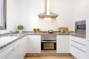 A modern kitchen with white cabinets, granite countertops, a stainless steel range hood, an oven, and a microwave. - Genteel Home San Gregorio (Seville)