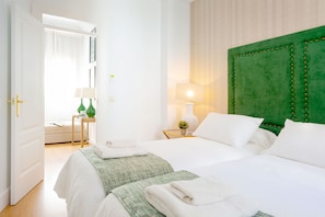 A hotel room with two beds, a green upholstered headboard, a bedside table with a lamp, and a view of a bathroom. - Genteel Home San Gregorio (Seville)