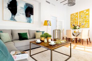 A living room with a sofa, coffee table, and chairs, a dining area with a glass table, and two large paintings on the wall. - Genteel Home San Gregorio (Seville)