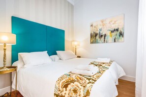 Ein Hotelzimmer mit Bett, zwei Nachttischlampen, einem Bild an der Wand und einem Fenster mit Vorhängen.