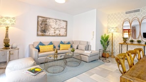 Ein modernes Wohnzimmer mit Sofa, Couchtisch, Hocker und Essbereich mit Stühlen.