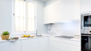 A modern kitchen with white cabinets, a built-in oven, and a window with blinds. - Genteel Home Encarnacion (Seville)