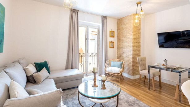 A modern living room with a sofa, a round glass coffee table, a wicker chair, a dining table with chairs, and a TV mounted on the wall. - Genteel Home Francos VII (Seville)