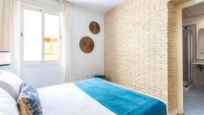 A bedroom with a bed, a window with curtains, a brick wall, and a shower area. - Genteel Home Francos VII (Seville)