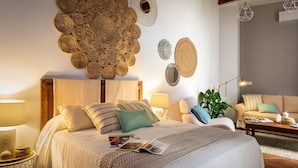 A well-lit bedroom with a large bed, a bedside table, a reading lamp, and a wall decorated with woven art pieces. - Genteel Home Casa Alhóndiga Terrace (Seville)
