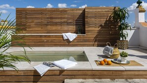 Une terrasse en bois avec une piscine, une serviette, une plante et un panier.