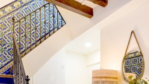 A staircase with blue steps and a wooden handrail, leading to a room with a white door, a lamp, and a green vase. - Genteel Home Galera Terrace (Seville)