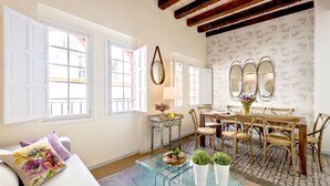 A spacious living room with a glass coffee table, a dining area with wooden chairs, and large windows with shutters. - Genteel Home Galera Terrace (Seville)