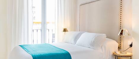 Ein Hotelzimmer mit einem großen Bett, einem Nachttisch mit Lampe, einem gemusterten Teppich und Blick nach draußen.