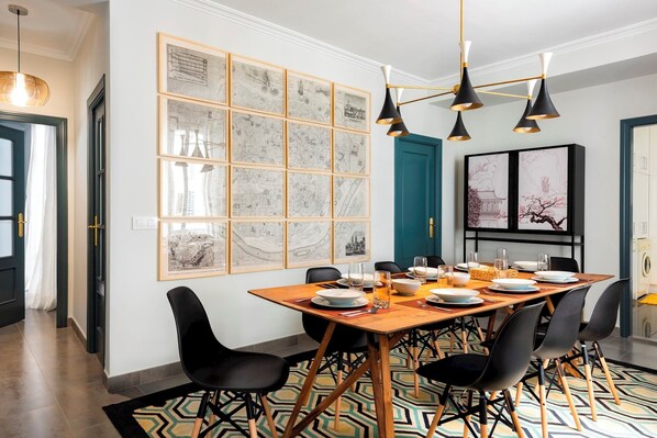 Un coin repas avec une table en bois, des chaises noires, un tapis à motifs et des cartes encadrées accrochées au mur.