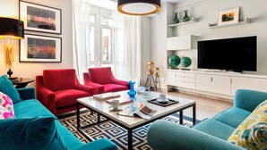 A modern living room with a large flat-screen TV, red and blue sofas, a coffee table, and decorative items. - Genteel Home Albareda (Seville)