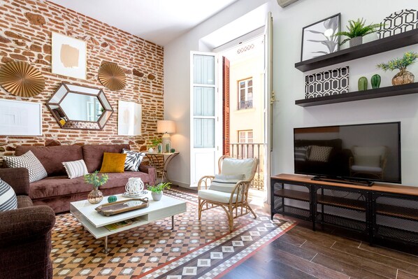 Un salon avec un mur en briques, un canapé, une table basse, un téléviseur et un tapis à motifs.