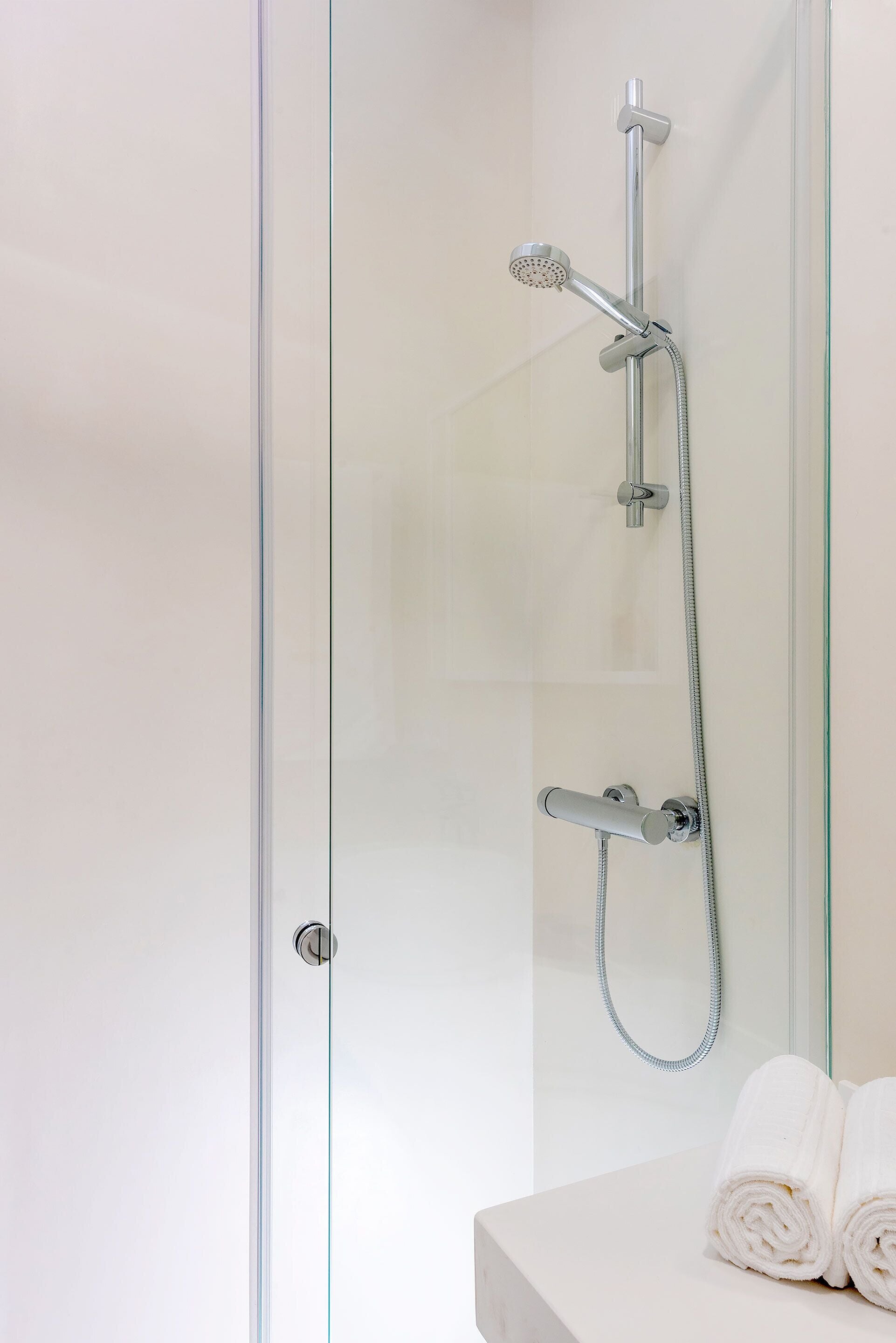 A modern bathroom with a glass shower enclosure, a handheld showerhead, a fixed showerhead, and a towel on a white countertop.