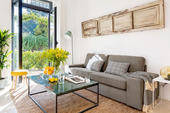 Een moderne woonkamer met een glazen salontafel, een grijze bank en uitzicht op groen.