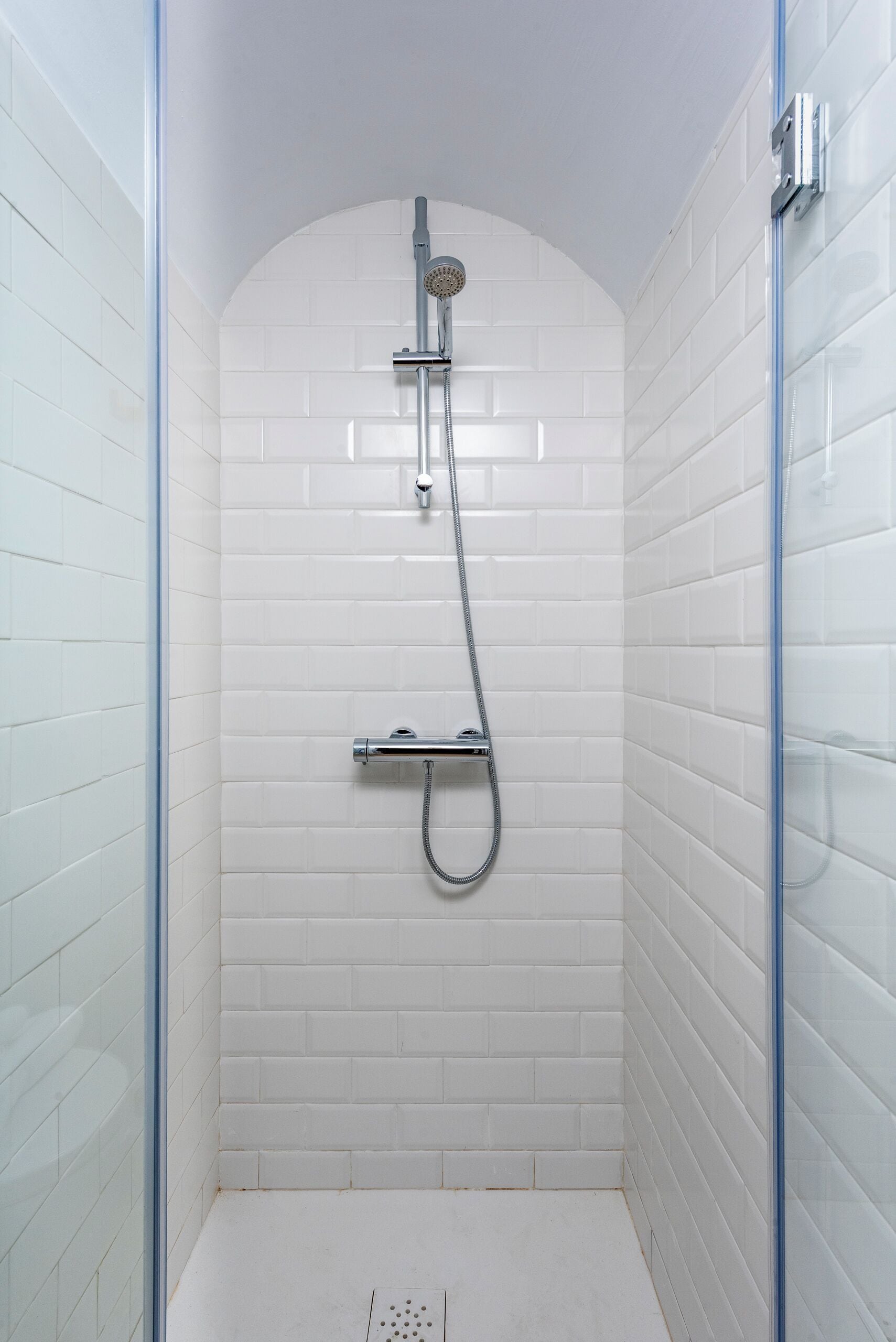 Un bagno doccia piccolo, con piastrelle bianche, una porta in vetro e un soffione a parete.