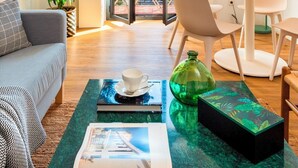 A modern living room with a sofa, a coffee table, a dining table with chairs, a potted plant, and a view through a glass door. - Genteel Home Santa Teresa (Seville)