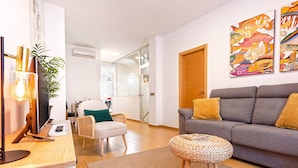 A modern living room with a grey sofa, a wicker ottoman, a white armchair, and a glass partition wall. - Genteel Home Don Pelayo (Seville)