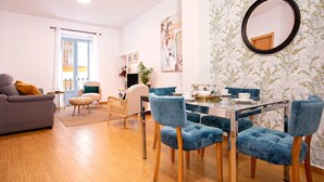 A modern living room with a glass dining table, blue upholstered chairs, a grey sofa, and a large mirror on the wall. - Genteel Home Don Pelayo (Seville)