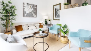 A modern living room with a white sofa, a round coffee table, and two armchairs. There are potted plants and framed artwork on the walls. - Genteel Home Mateos Gago IV (Seville)