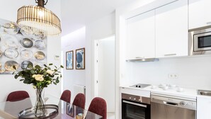 A modern kitchen with white cabinets, stainless steel appliances, and a glass dining table with red chairs. - Genteel Home Mateos Gago IV (Seville)