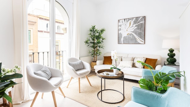 A modern living room with a white sofa, two armchairs, a coffee table, and a view of the city through large windows. - Genteel Home Mateos Gago IV (Seville)