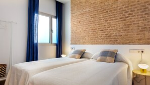 Une chambre avec deux lits, un mur en briques, une fenêtre avec des rideaux bleus et une table de chevet avec une lampe.