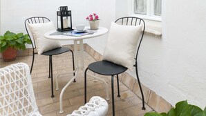 A small patio area with a round table, two chairs, a potted plant, and a window with curtains. - Genteel Home Conde de Ibarra (Seville)