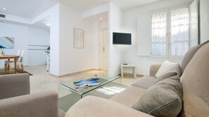 A modern living room with a glass coffee table, beige sofa, and a flat-screen TV mounted on the wall. - Genteel Home Conde de Ibarra (Seville)