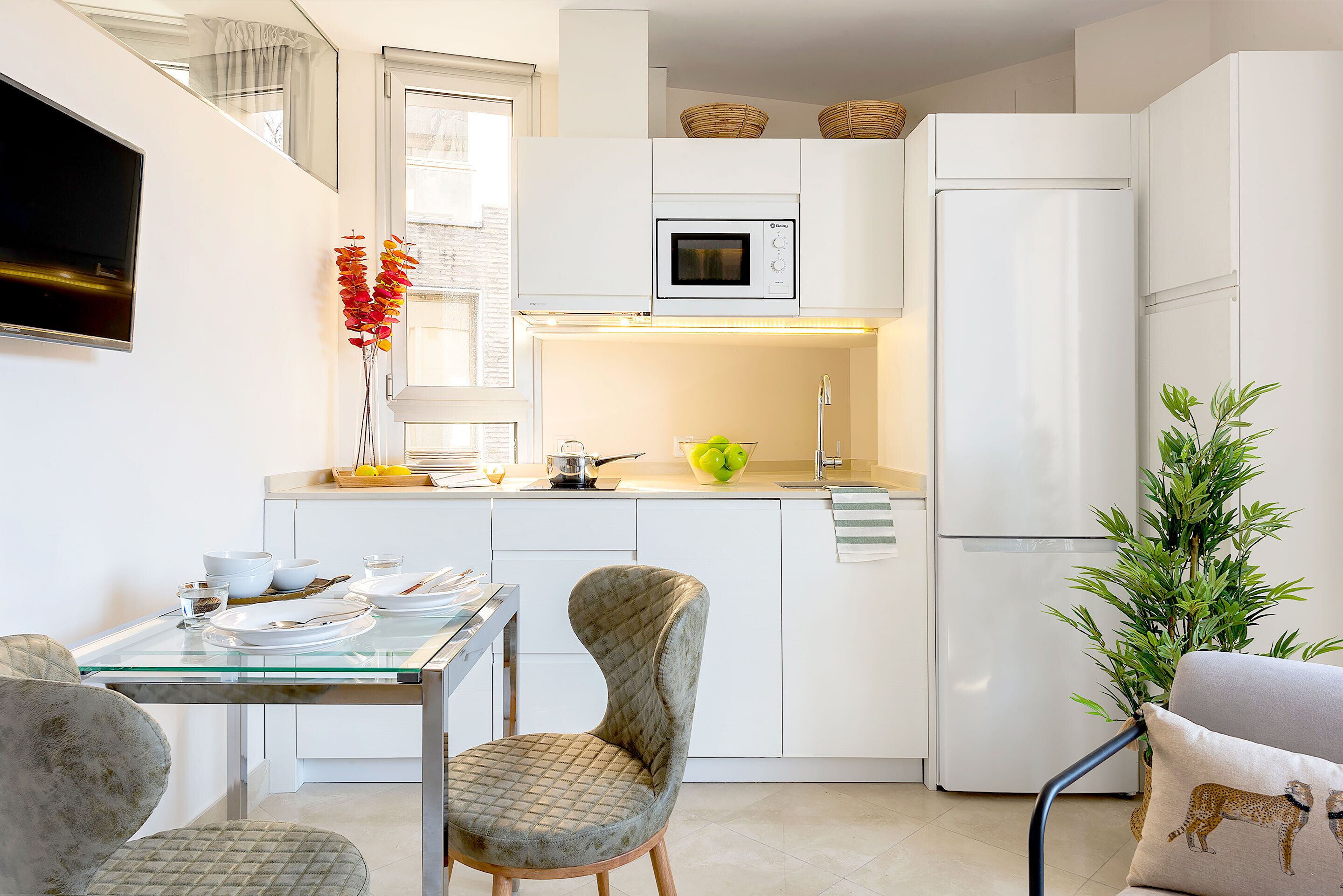 A modern kitchen with white cabinets, a microwave, a refrigerator, and a dining area with a glass table and chairs.