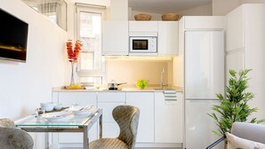 Eine moderne Küche mit weißen Schränken, einer Mikrowelle, einem Kühlschrank und einem Essbereich mit einem Glastisch und Stühlen.
