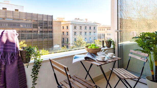Ein Balkon mit einem Tisch für zwei Personen, einer Zeitschrift, einer Schüssel Äpfel und einem Blumentopf.