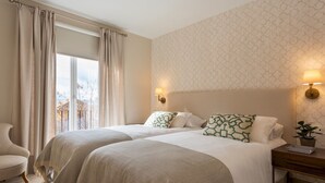 Habitación de hotel con dos camas, una silla, una mesita de noche y vistas al exterior.