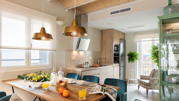 Una cocina moderna con armarios de madera, horno empotrado y comedor con mesa de madera y sillas azules.